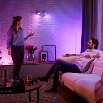 Un couple se détend dans un salon éclairé avec une lumière violette et rose projetée par des lampes connectées Philips Hue. 