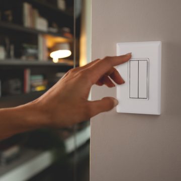 Hand, die einen weißen smarten Schalter an der Wand einschalten möchte