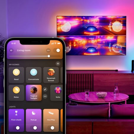 Ein farbig beleuchteter Raum mit einem an der Wand montierten Fernseher, auf dem ein Rennspiel mit geteiltem Bildschirm angezeigt wird. Ein Overlay der Hue App zeigt die Registerkarte Home an.