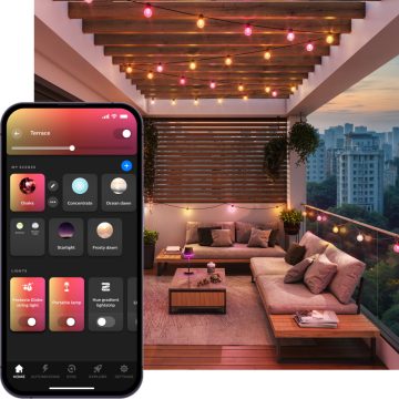 A balcony seating area at night lit with strings of Festavia outdoor globe party lights glowing in pink and yellow tones of smart light. 