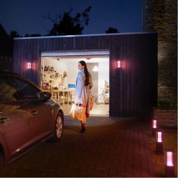 Woman walking from car to brightly lit garage with bag of groceries