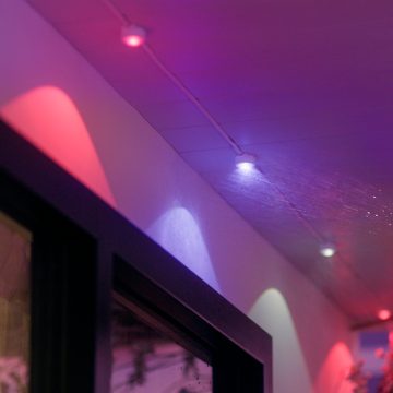 A string of Festavia permanent lights attached to a balcony ceiling with light pods glowing in pink and purple light