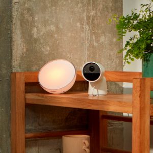 A Hue Secure camera and lamp on a piece of wooden furniture.
