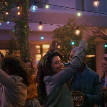 A woman dances on a patio under strings of Festavia outdoor globe party lights glowing in blue, pink and white smart light.