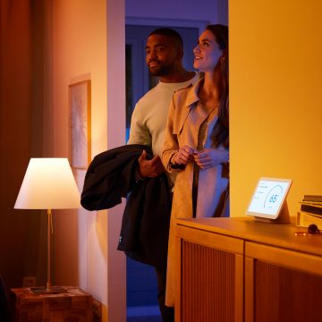 A couple enters a living room glowing in warm white smart light.