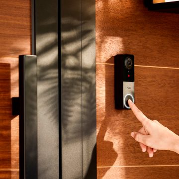 A finger pressing the button of a Wired video doorbell mounted to a wall