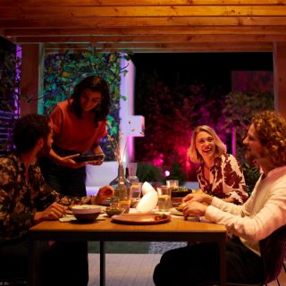 A group of friends enjoy a meal outside on a patio decorated with colorful smart light.
