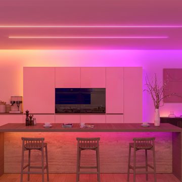 A kitchen lit in vibrant pink and orange tones of light using a combination of concealed strip lights behind ceiling coves and visible strip lights on the ceiling. 