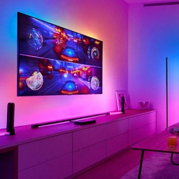 A racing game appears on a large TV screen hanging on a wall with synced-up surround lighting around it.