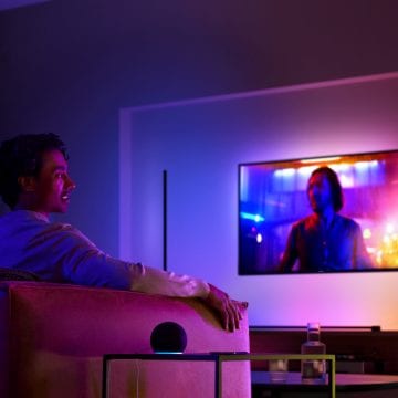Man on a couch watching TV with surround lighting and a smart speaker on the side table next to him