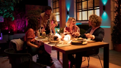 A group of friends enjoy an outdoor dinner party illuminated with colorful outdoor smart lighting available in the outdoor smart lighting sale. 