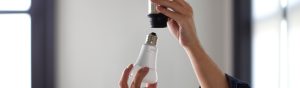 Hand installing a white smart light bulb into a socket, focusing on the bulb and the action of screwing it in for setup.