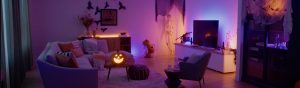 Living room decorated for Halloween with soft ambient glow in purple and orange, jack-o'-lantern and skeleton visible.