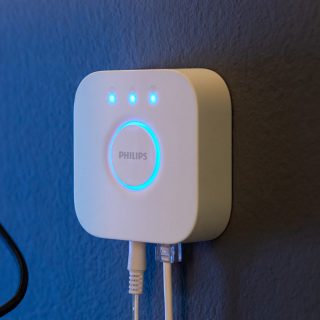 White smart home bridge mounted on a wall, showing blue indicator lights and connected cables, enabling smart lighting control.