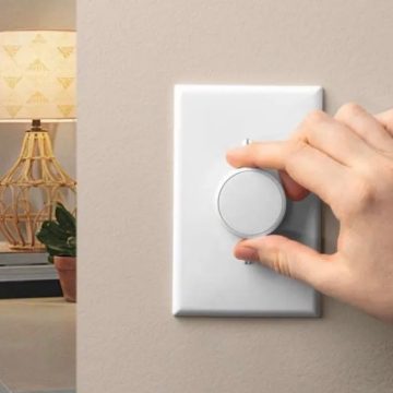 Hand turning the dial of a white smart home light switch on wall