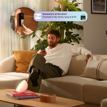 A man sits on his sofa receiving a detection notification on his smartphone via the Hue app. 