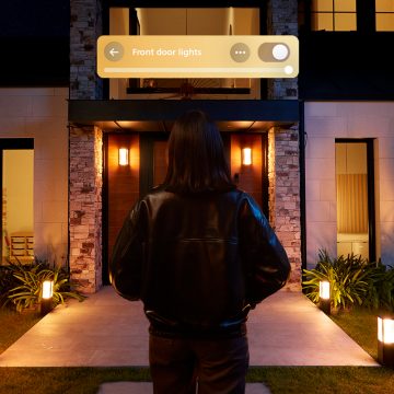 A person approaches the front door of a home triggering Philips Hue lights via a video doorbell. 