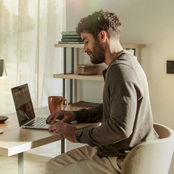 A man sits working at his laptop and monitors his front door via A Hue Doorbell live feed.