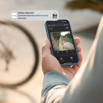 A person monitors their front door with a Hue Secure video doorbell via the Hue app while away from home. 