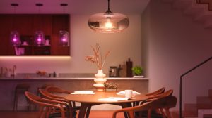 Pendant light with glass shade suspended above dining table, casting neutral light onto tableware and decorative vase.