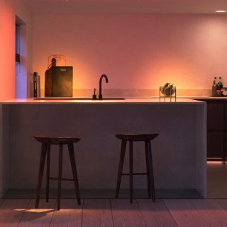 Smart lighting illuminates a kitchen countertop with a sink, stools, and visible fruit bowl, highlighting functional areas.