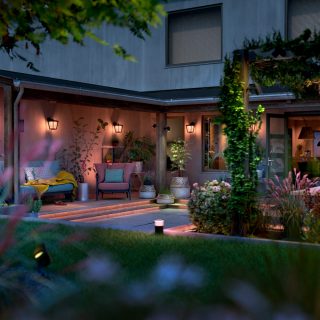 Outdoor smart wall lights and pathway lights illuminate a backyard patio, highlighting seating, plants, and garden features.