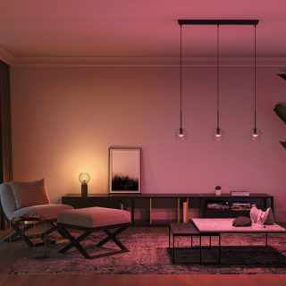 Pendant smart lights with clear glass shades are suspended from the ceiling, casting colored illumination over a living room.