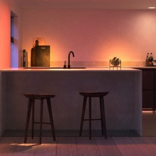 Smart kitchen lighting illuminates countertop and backsplash, highlighting sink area, fruit bowl, and kitchen accessories with colored light.