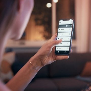 Een vrouw met in haar hand een telefoon met app voor slimme lampen