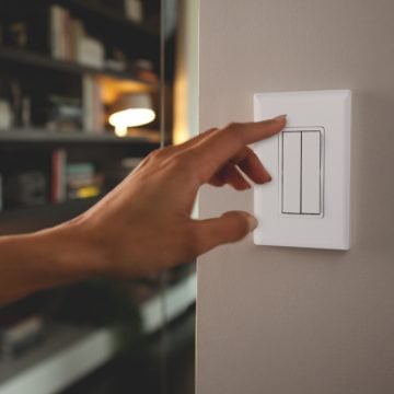 Hand die aan de knop gaat draaien van een witte slimme lichtschakelaar op de muur