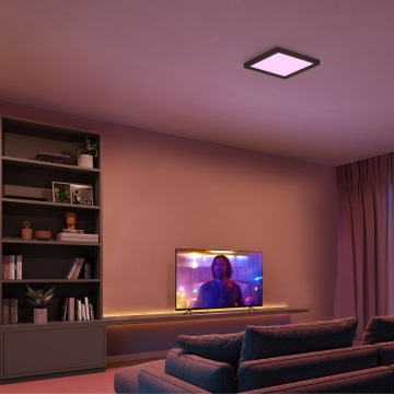 Zwarte, vierkante plafondlamp ingesteld op paars licht in een woonkamer met een tv