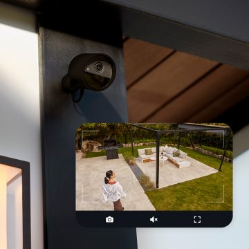 Et Hue Secure-kamera festet til en vegg og et livebilde fra kameraet som viser en kvinne i en bakgård.