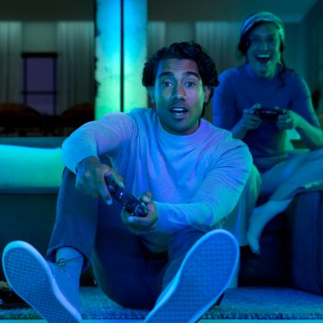 En gamer spiller et spill på et trippel monitor oppsett ved hjelp av Hue gradient lightstrips og light bars. 