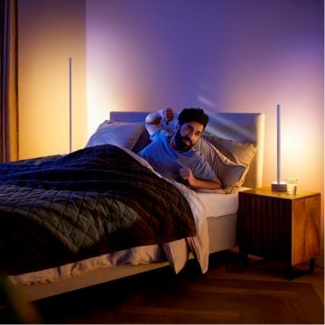 Homem se espreguiçando na cama com piso inteligente e lâmpadas para mesa suavemente iluminadas 