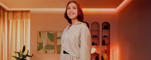 Uma mulher está de pé numa sala de estar iluminada por luzes e candeeiros Philips Hue.